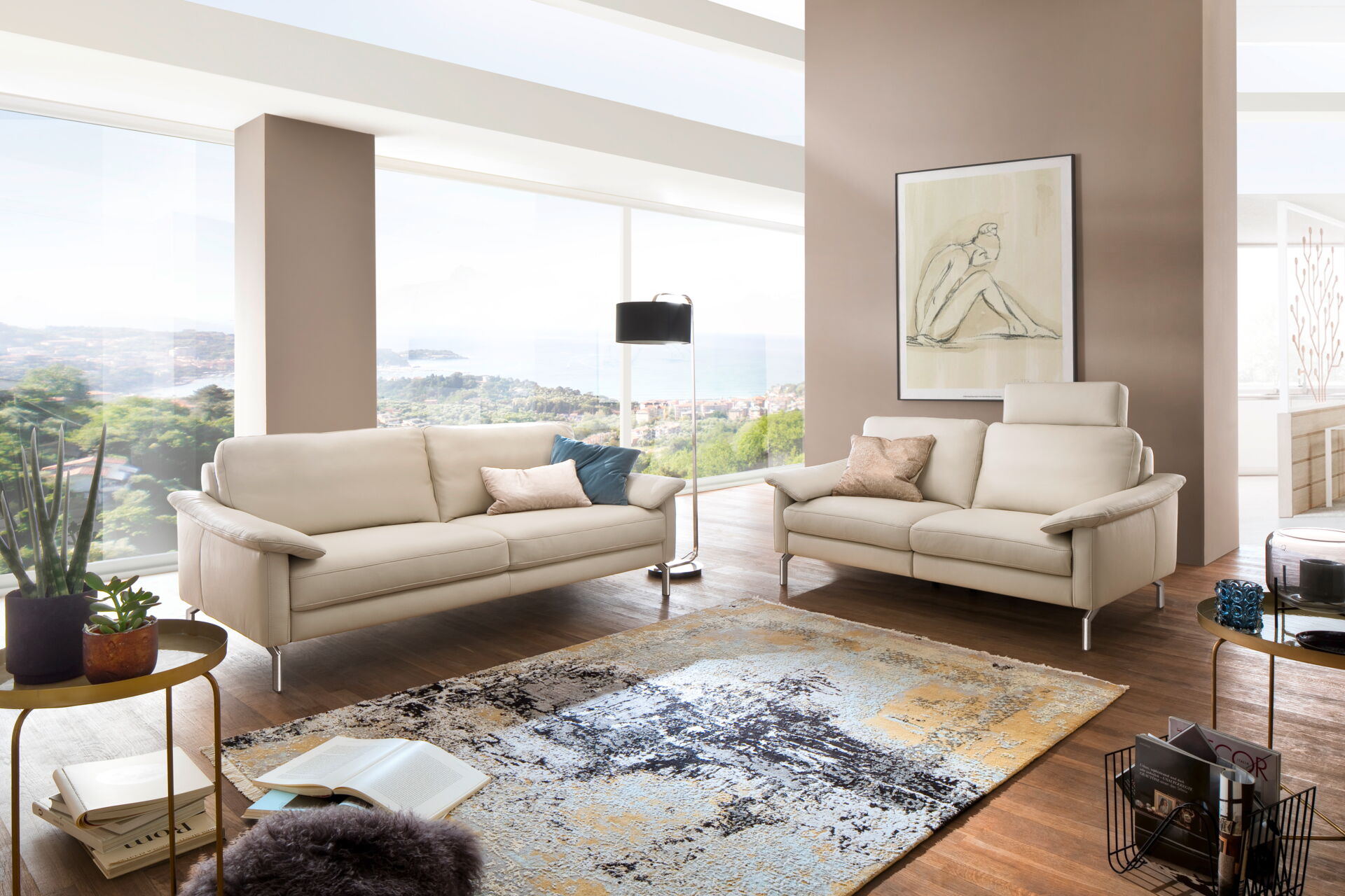 Ein elegantes Wohnzimmer mit beigem Sofa und Zweisitzer, Teppich und großen Fenstern, eingerichtet mit Möbeln von Möbel Lutz aus Obernbreit.