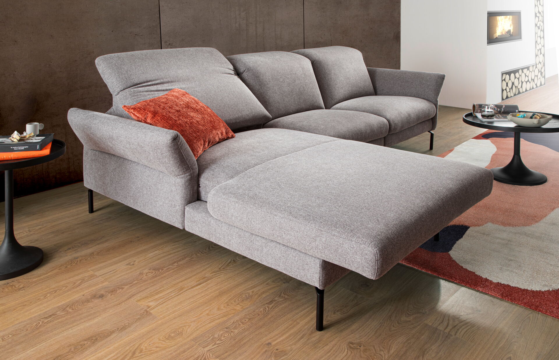 Ein elegantes, hellgraues Sofa mit Relaxfunktion und einem roten Kissen, inspiriert von Möbel Lutz aus Obernbreit.